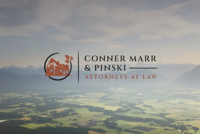 Logo of Conner Marr & Pinski, Attorneys at Law, featuring an illustration of a house with a tree inside a circular design, set against a blurred aerial landscape of fields and mountains