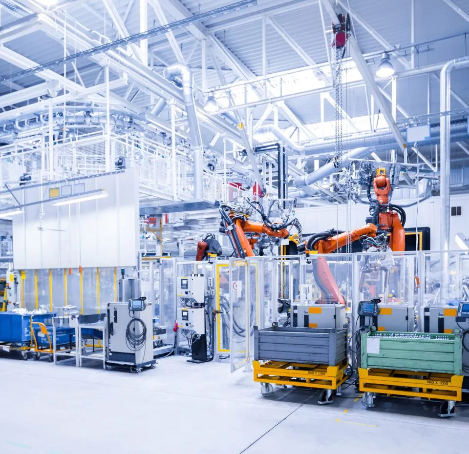 A bright, high-tech factory floor featuring multiple large, orange robotic arms working on an assembly line, surrounded by white structural components and machinery.