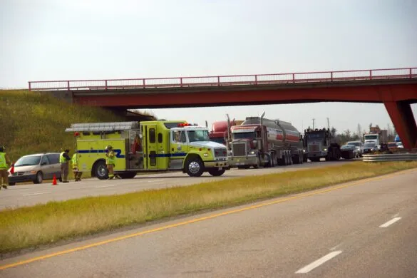 Emergency services, including a lime green fire truck, attend to a severe traffic accident involving multiple large tractor-trailers and cars beneath a red highway overpass.
