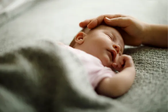 An image of a sleeping newborn with a hand gently touching the baby’s head.