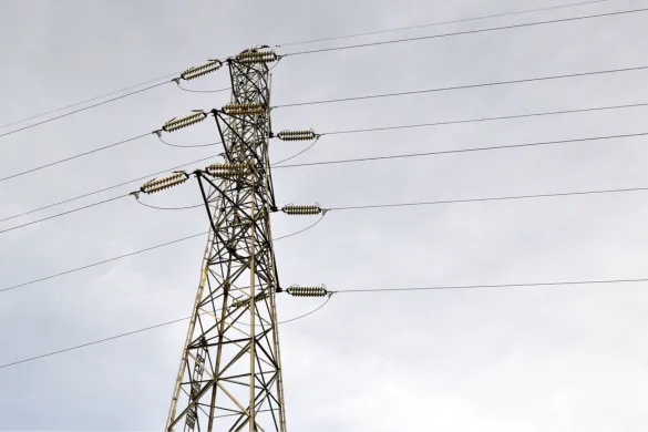 A large metal electrical transmission tower (pylon) carrying high-voltage power lines across a cloudy sky.