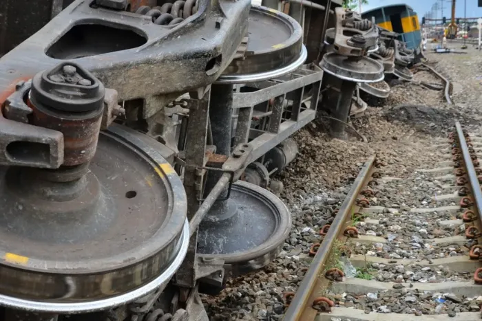 Heavy metal wheels and undercarriage of a rail car lying tilted off the track after a train derailment.