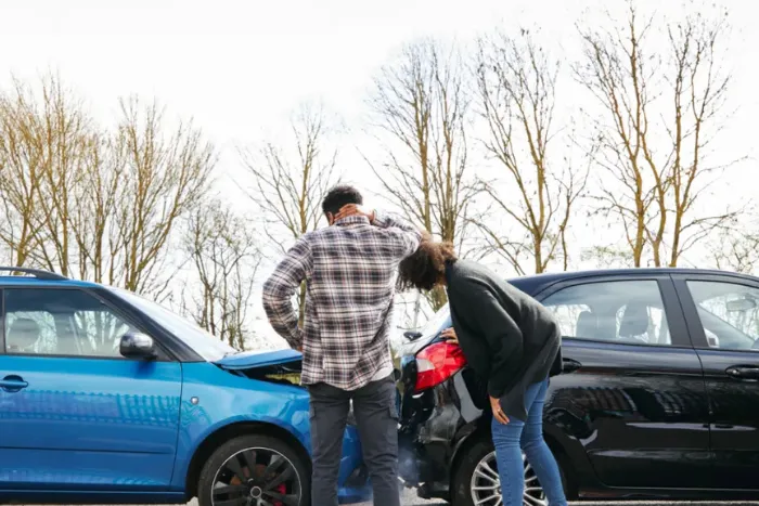 Two people, a man and a woman, standing outside their cars in the aftermath of a minor rear-end car accident.