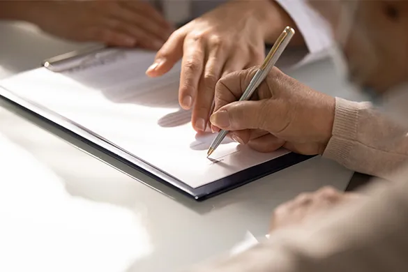 An image of two hands, one guiding and the other signing a document.