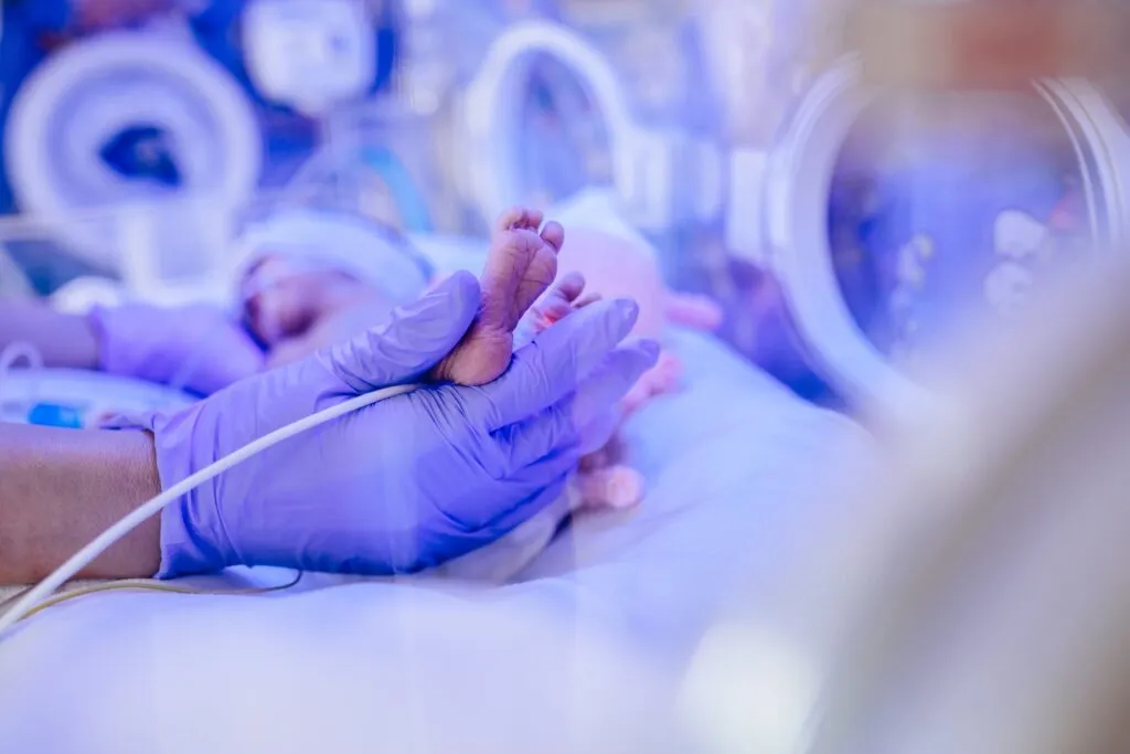 A nurse wearing purple medical gloves, is gently holding the baby's tiny feet.