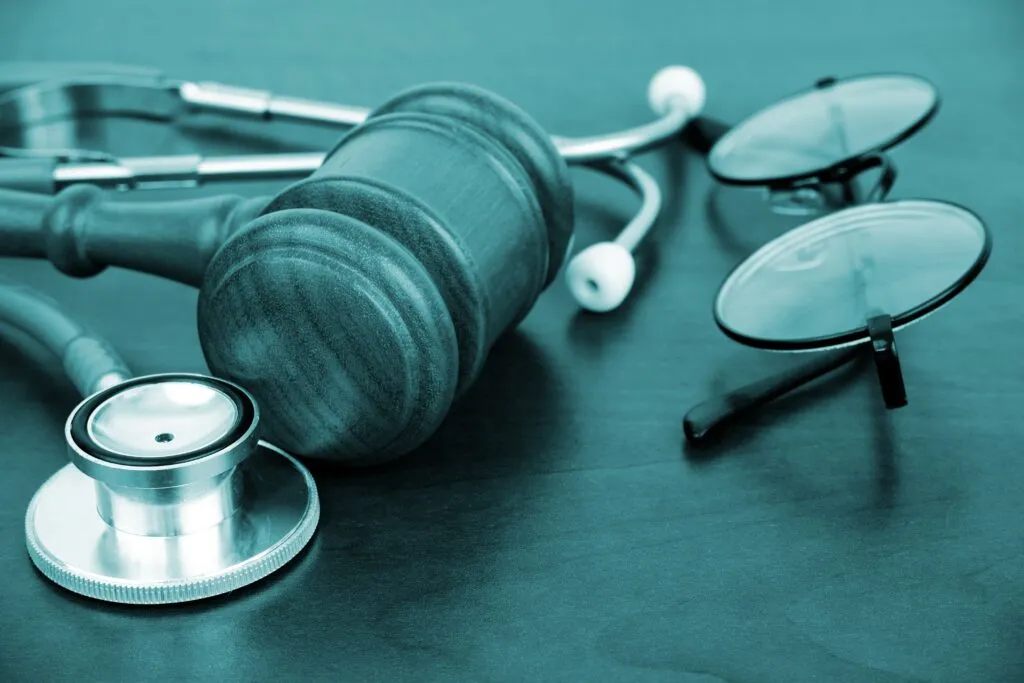 A wooden gavel and a stethoscope resting on a dark surface, symbolizing the intersection of law and medicine.